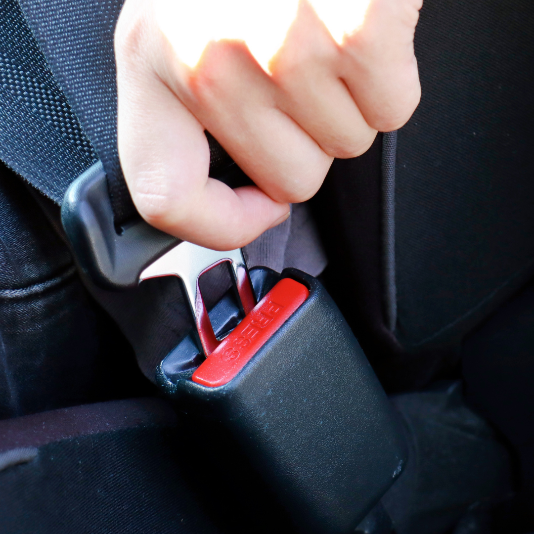 A hand inserting the metal tongue into a seatbelt buckle.